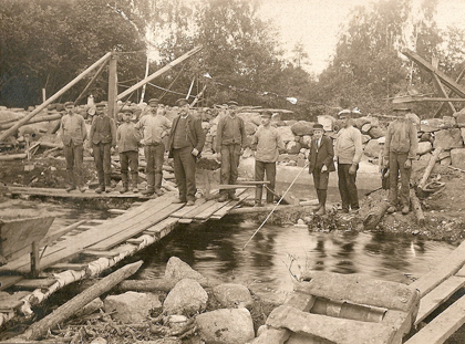 Carl Fritjof Lund (hitom skottkärran) leder arbetet med dammbyggnaden i början av 1909. Sonen John med slips och knäbyxor ägnar sig åt fiske.