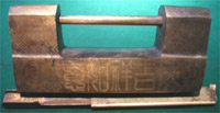 Large box-shaped lock of bronze with etched text; frontsides are shown. Note the coin designs.